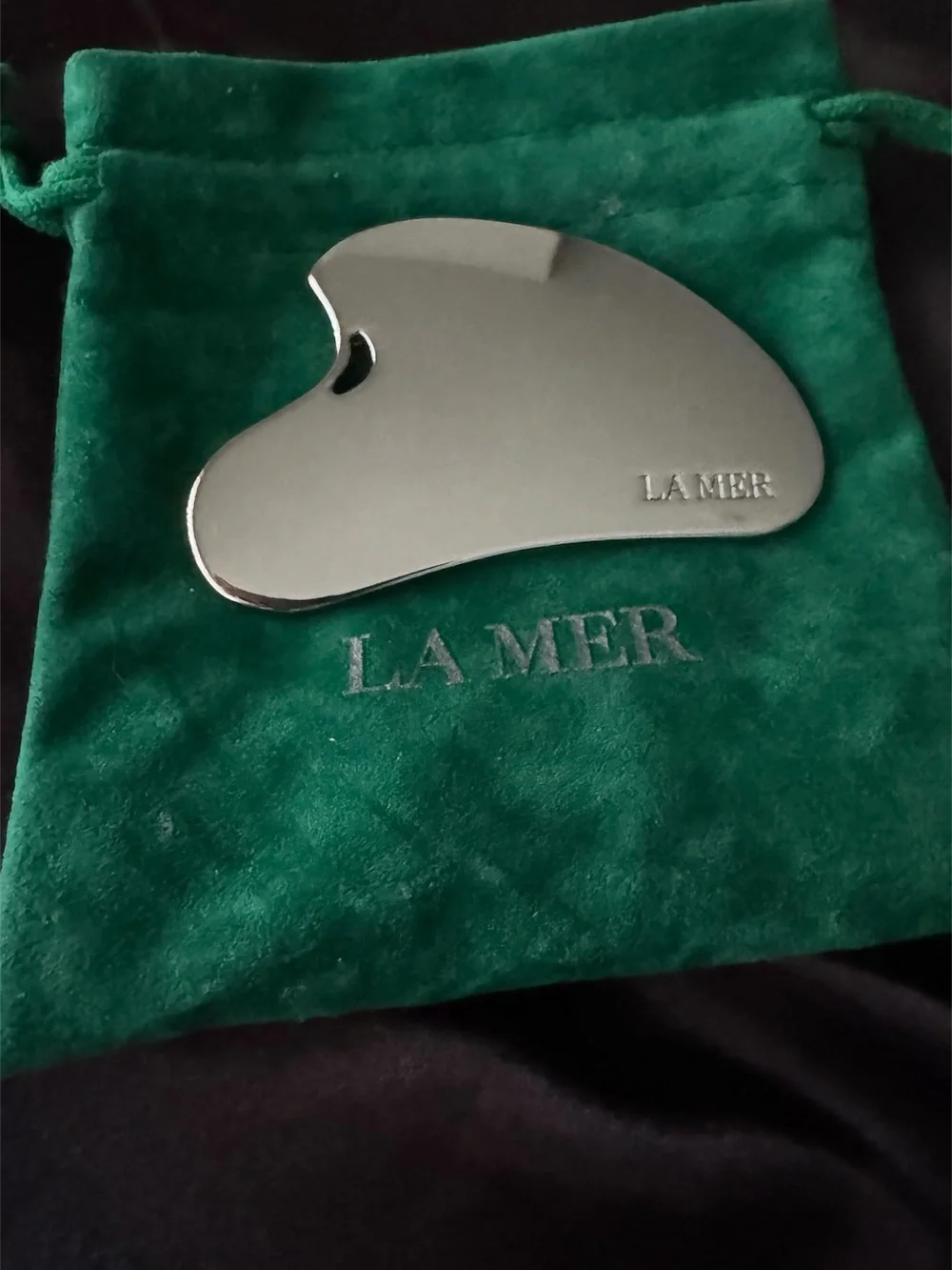 La Mer Silver Stainless Steel Gua Sha on Green Velvet Pouch and cosmetic bag